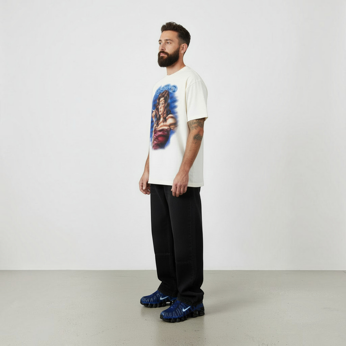 NDO Clothing T-Shirt in creme mit grafischem Pin-up-Print auf der Vorderseite, getragen von einem bärtigen Model.